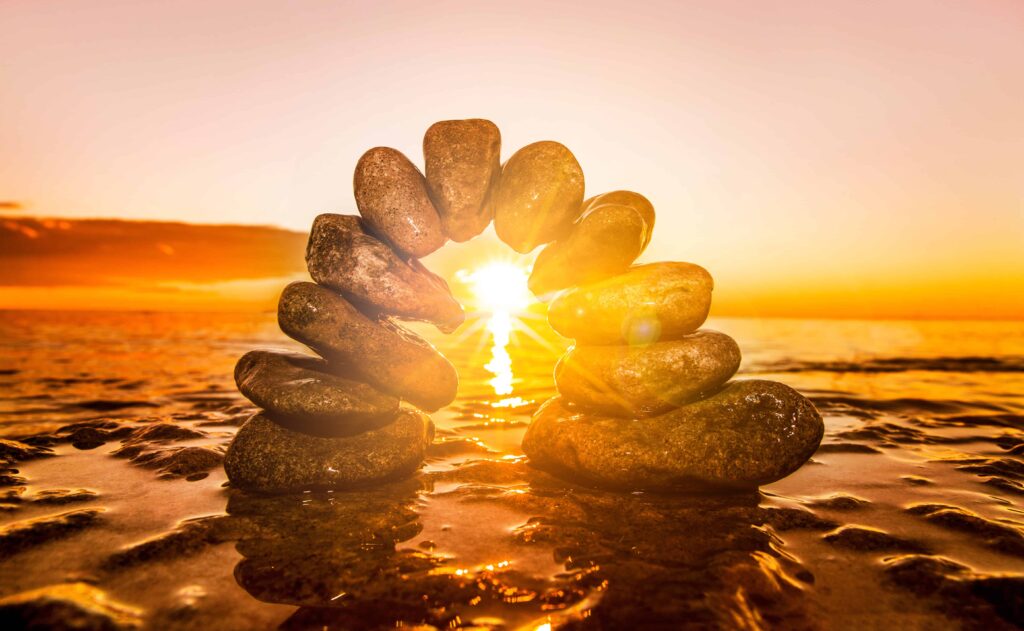 Image of balancing rocks on a beach with the sunrise shining through - signifying health, wellness and balance.
