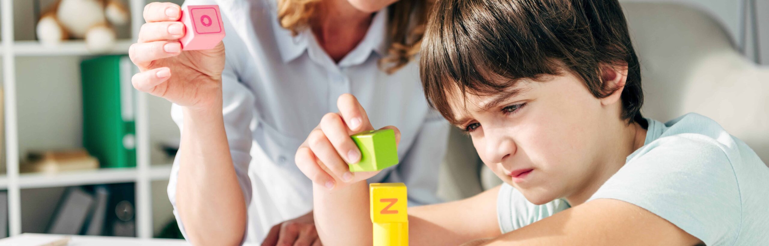 Boy with autism building blocks with a carer supporting him.