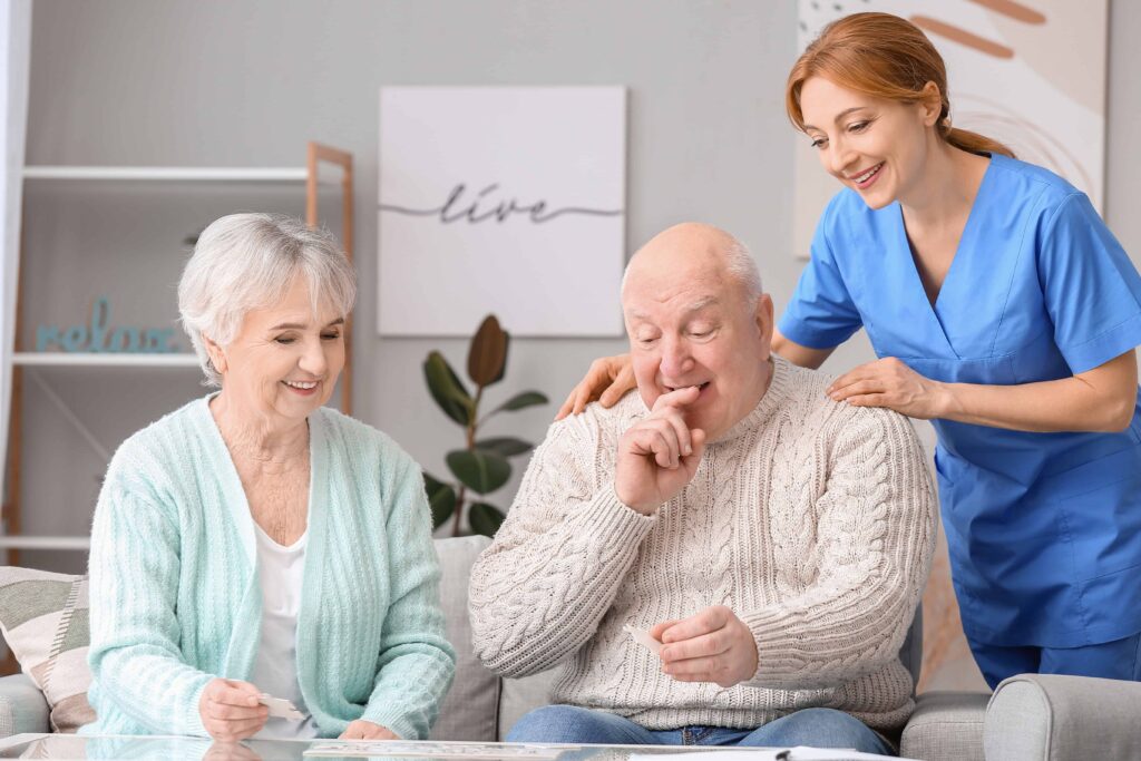 Man with Parkinsons being encouraged by a carer and his wife to build a puzzle. All look happy and encouraged.
